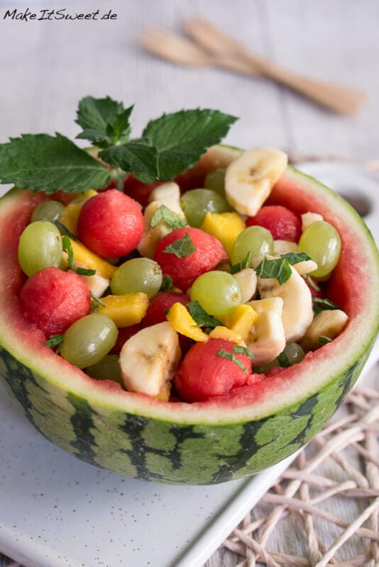 Wassermelonen Obstsalat in einer halben ausgehöhlten Wassermelone mit Banane, Trauben und Mango sowie Minze